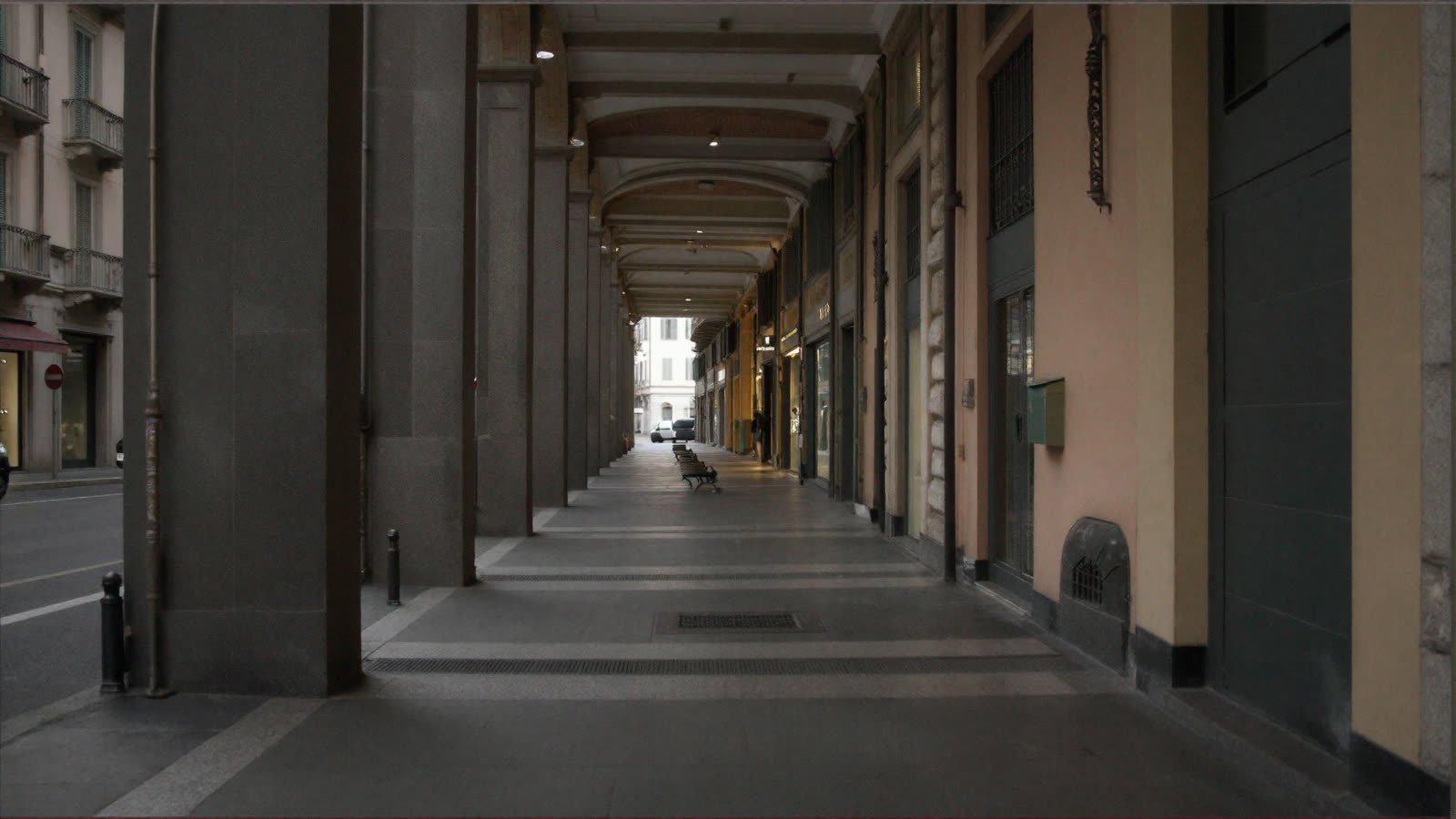 A camera standing inside the portico: piers to the left with the cold street between them, shopfronts to the right, groin vaults overhead