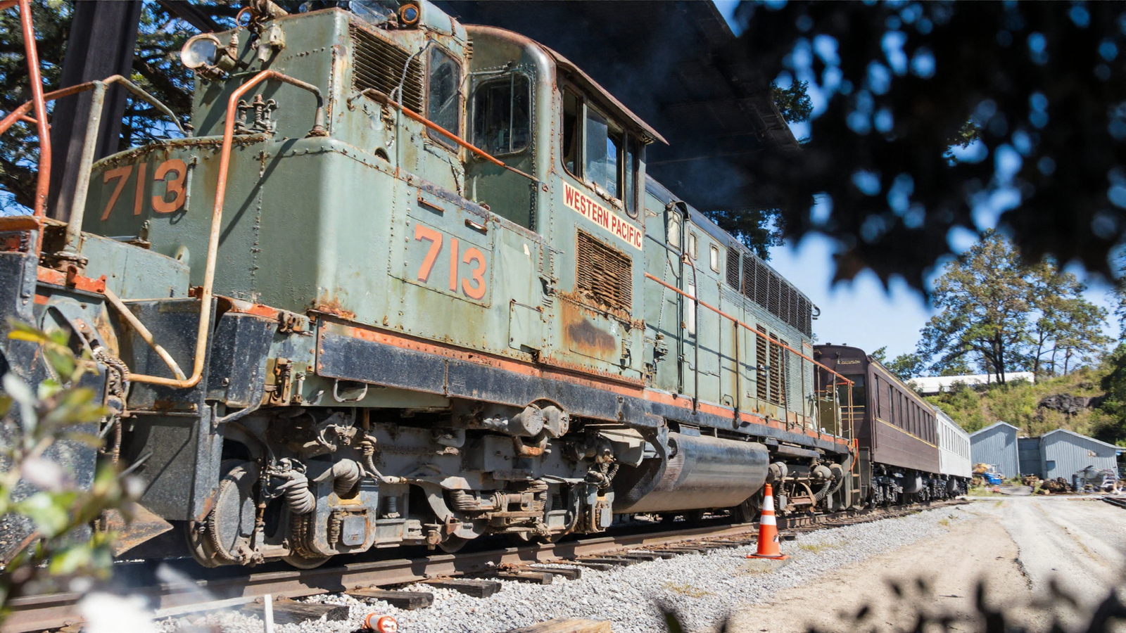 A dramatic low-angle photograph of the same green locomotive taken from rail level looking up along its flank, showing the number 713 and the words Western Pacific, with the orange traffic cone still beside the track.