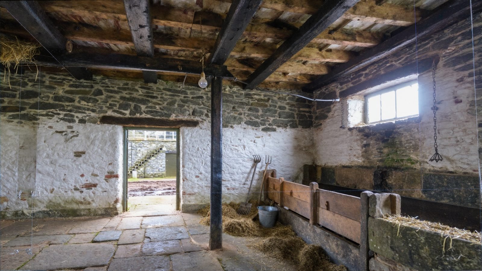 Inside a stone byre looking out through the open door to a muddy yard
