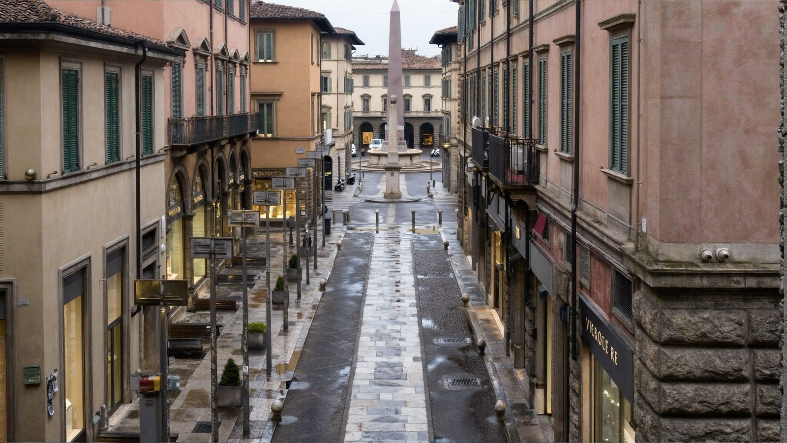Looking down an Italian shopping street to a stone obelisk in a circus