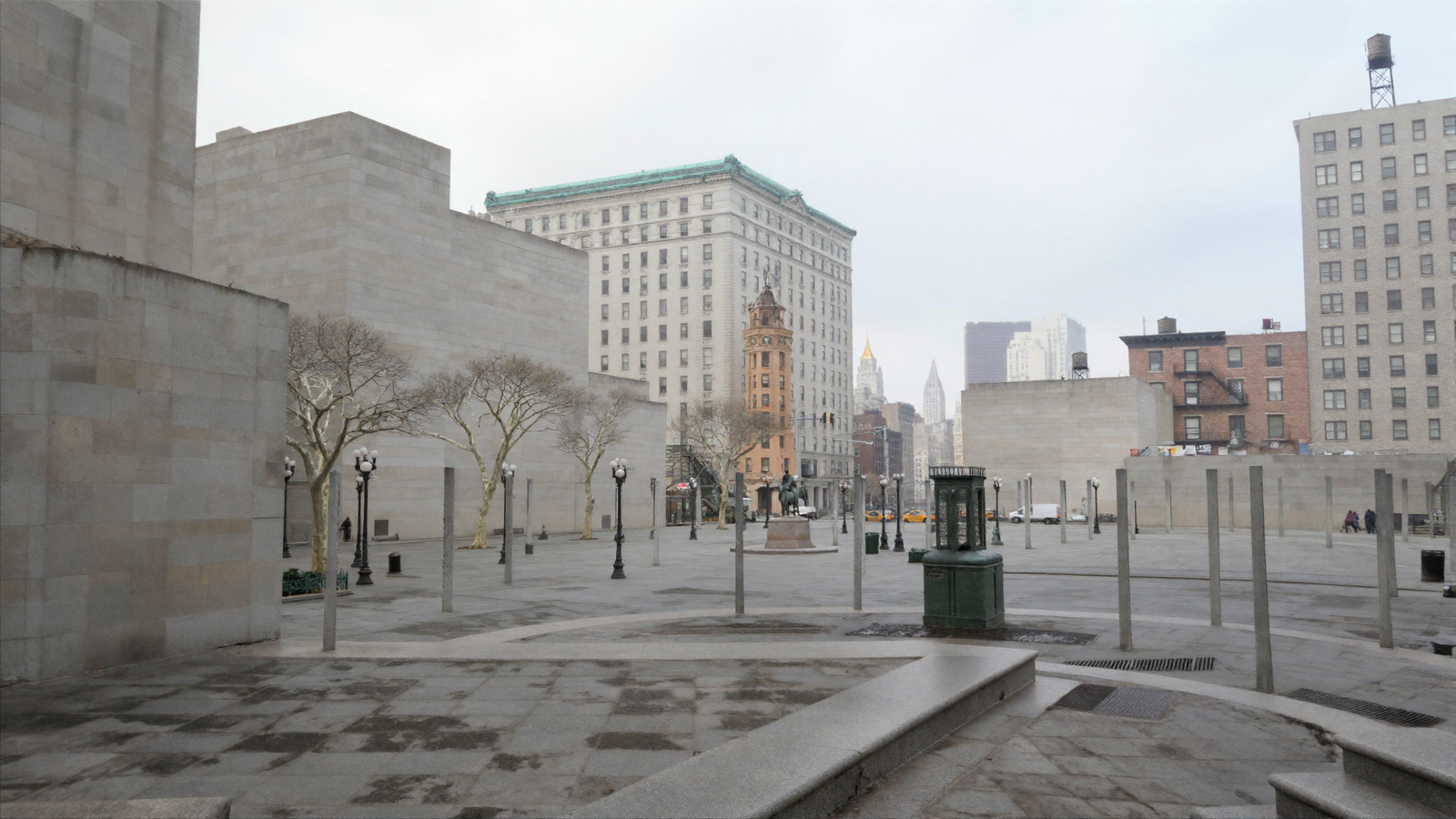 A photorealistic overcast view across a granite plaza toward a park of bare winter plane trees, with a bronze equestrian statue on a plinth, an ornate terracotta tower and a limestone building with a green copper cornice behind, and a gold-crowned tower in the far haze. Plain grey posts still stand in rows across the plaza and the nearest buildings are blank windowless walls.