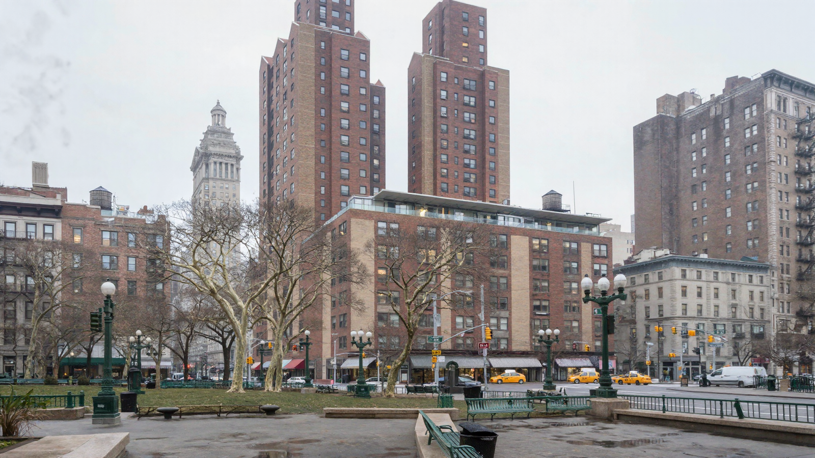 A photorealistic overcast view across Union Square toward Zeckendorf Towers: stepped red-brown brick towers with buff panels rising from a broad brick base block with a glass-walled rooftop terrace, a classical clock tower to the left, bare plane trees, green cast-iron globe lampposts and benches, yellow taxis and awnings at street level.