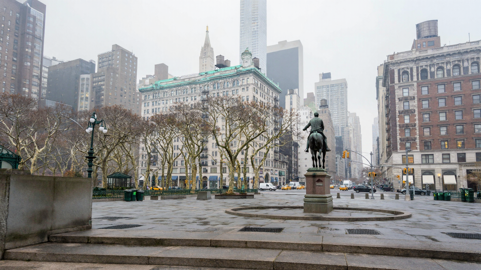 A photorealistic overcast view north across Union Square: a bronze equestrian statue on a granite plinth standing in a circular paved surround, a ring of concentric paving across the plaza, broad granite steps in the foreground, dense bare plane trees, a green-roofed pavilion, a limestone building with a green copper cornice, water tanks on the roofs, and the gold-crowned Metropolitan Life campanile in the haze behind.